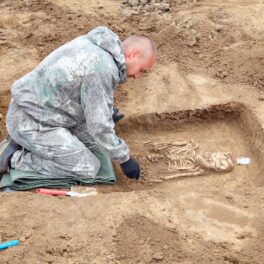 Arheolog care excavează și analizează un schelet, cu pământ bej pe lângă, similar cu sute de schelete găsite în Țara Galilor