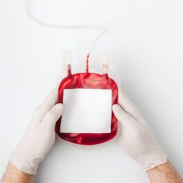 Pungă de transfuzie de sânge, ținută în mâna unei persoane care poartă mănuși, pe fundal alb. Recent, experții au găsit un nou tip de sânge rar