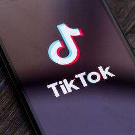 Emblema TikTok pe ecranul unui telefon, pe fundal de lemn închis. Compania a declarat recent că angajații TikTok din China pot accesa datele utilizatorilor din Europa