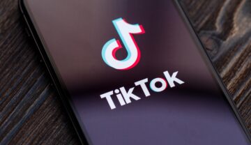 Emblema TikTok pe ecranul unui telefon, pe fundal de lemn închis. Compania a declarat recent că angajații TikTok din China pot accesa datele utilizatorilor din Europa