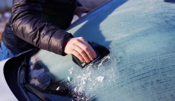 Bărbat care șterge cu racleta parbrizul înghețat al mașinii. Experții au dezvăluit cum să dezgheți parbrizul mașinii rapid