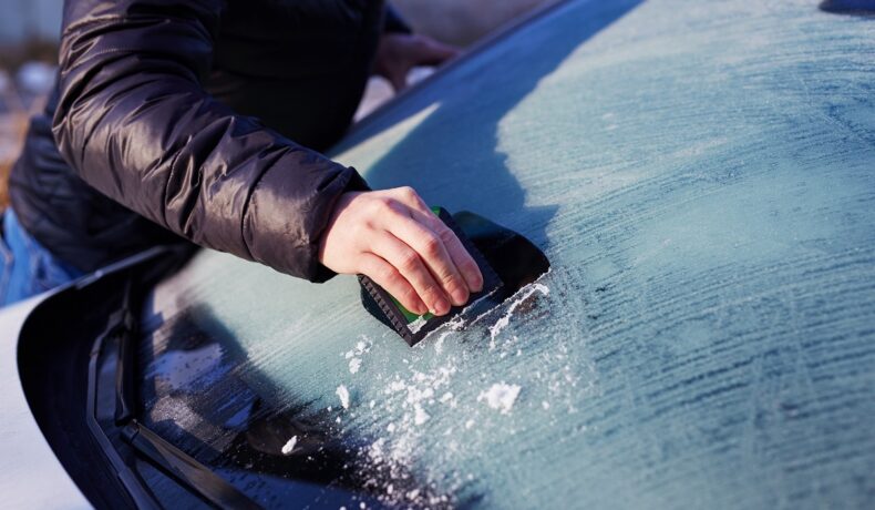 Bărbat care șterge cu racleta parbrizul înghețat al mașinii. Experții au dezvăluit cum să dezgheți parbrizul mașinii rapid