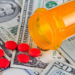 Imagine cu un tub galben de pastile, cu pastile roșii peste dolari, care nu seamănă cu cel mai scump medicament din lume