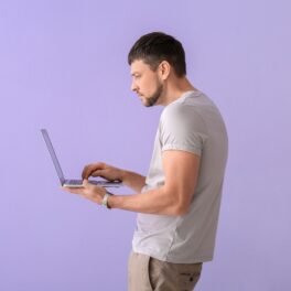 Bărbat care se uită în laptop, pe fundal mov. EXperții susțin că corpul oamenilor ar putea fi deformat din cauza tehnologiei