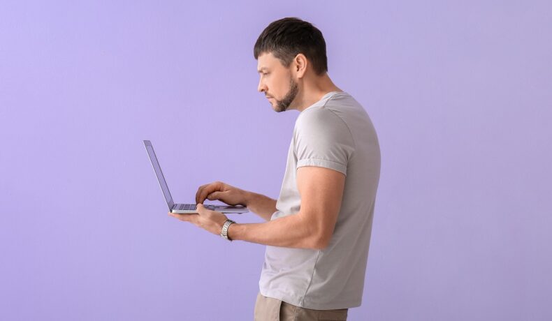 Bărbat care se uită în laptop, pe fundal mov. EXperții susțin că corpul oamenilor ar putea fi deformat din cauza tehnologiei