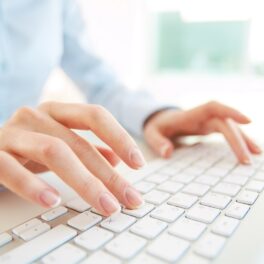 Persoană care scrie la o tastatură albă, îmbrăcată într-o cămașă albastră. A fost dezvăluit topul cu țările cu cel mai rapid Internet