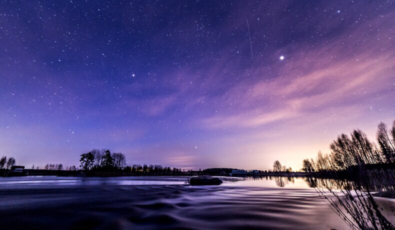 Peisaj de noapte, cu cerul mov și albastru, deasupra unui lac, similară cu cea mai lungă noapte din an
