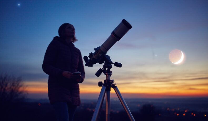Femeia care se uită printr-un telescop noaptea, similar cu fenomenul inedit care apare pe cer în ianuarie 2023