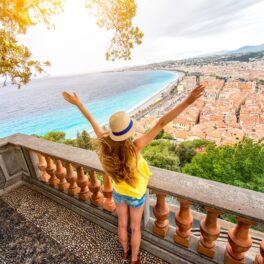Turistă în pantaloni scurți, tricou galben, care stă pe balcon și se uită la peisaj din Nisa, Franța, cea mai vizitată țară din lume