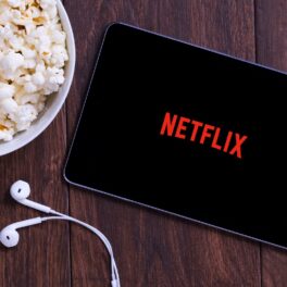 Tabletă Netflix, pe fundal de lemn, cu un bol de popcorn lângă. Compania a dezvăluit codurile secrete Netflix