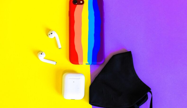 Telefon mobil în culori de curcubeu, pe fundal cu mov și galben, cu căști wireless albe și o mască neagră lângă. O nouă tehnologie explică cum poți schimba culoarea telefonului