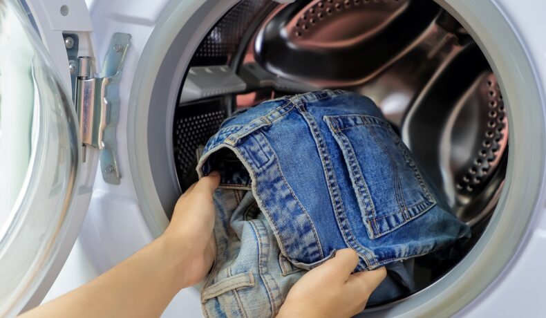 Persoană care folosește mașina de spălat și scoate blugi din ea. Experții au dezvăluit de câte ori poți purta blugii și alte haine înainte să le speli