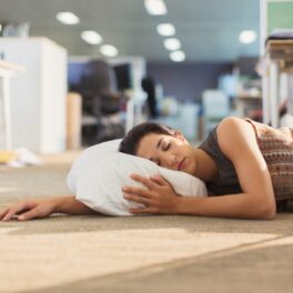 Femeie brunetă care dorme la birou, pe podea bej, cu o pernă albă, la fel cu directoarea Twitter care dormea la birou