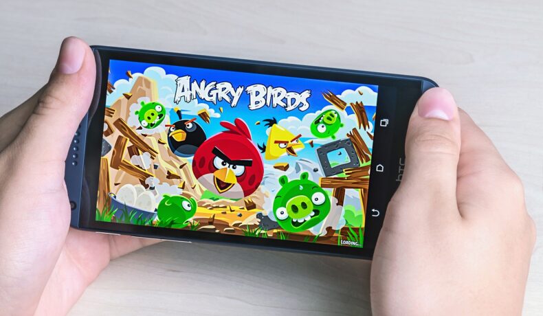 Utilizator care ține un telefon în mână cu jocul Angry Birds pe ecran, ce dispare din Google Play Store