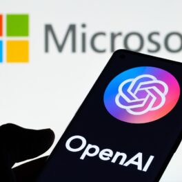 Logo-ul Microsoft și OpenAI, pe telefon, ținut în mână de cineva. Microsoft anunță acum integrarea tehnologiei ChatGPT