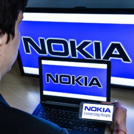 Utilizator în fața unui monitor de calculator, monitor de laptop și ecran de telefon. pe toate ecranele e vechiul logo Nokia, care a fost ănlocuit de noul simbol