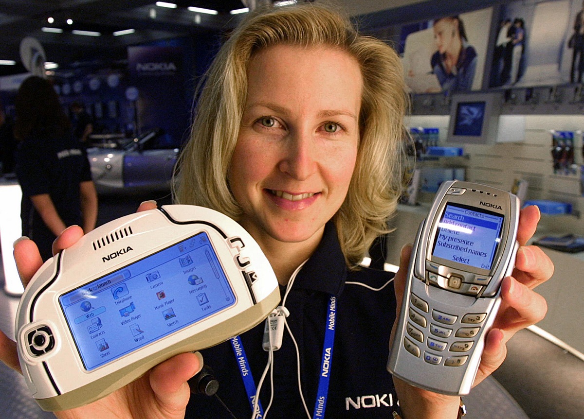 Femeie blondă care ține în mână modelele Nokia 7700 și 6810, care se numără printre telefoanele vechi care costă acum o avere
