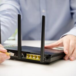 Utilizator care scoate cablu galben dintr-un router WiFi negru, pe o masă așbă, pentru a ilustra cât de des trebuie să oprești routerul WiFi