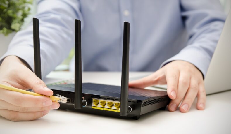 Utilizator care scoate cablu galben dintr-un router WiFi negru, pe o masă așbă, pentru a ilustra cât de des trebuie să oprești routerul WiFi