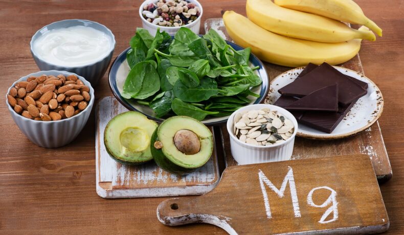 Alimente bogate ăn magneziu, precum banana, spanac, alune, avocado, pe o masă din lemn. Experții au vorbit despre ce efect are magneziul în corp