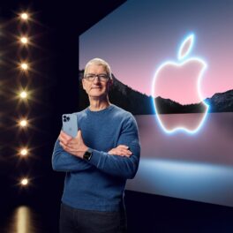 Tim Cook, CEO-ul Apple, cu logo-ul companiei pe fundal și un iPhone ăn mână. Casca virtuală e dispozitivul Apple pe care Tim Cook insistă să îl lanseze