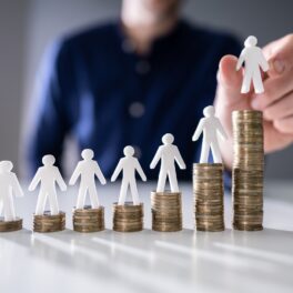 Persoană care pune figurine albe pe grămezi de monede, care simbolizează salariul minim pe economie în creștere
