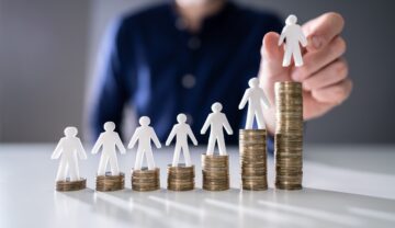 Persoană care pune figurine albe pe grămezi de monede, care simbolizează salariul minim pe economie în creștere