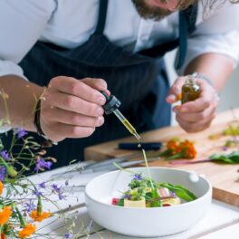 Bucătar care gătește o masă de lux, cu o pipetă de ulei deasupra unui castron alb cu salată, pentru a ilustra cel mai scump prânz