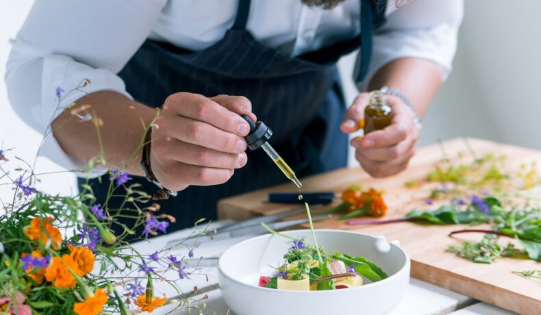 Bucătar care gătește o masă de lux, cu o pipetă de ulei deasupra unui castron alb cu salată, pentru a ilustra cel mai scump prânz