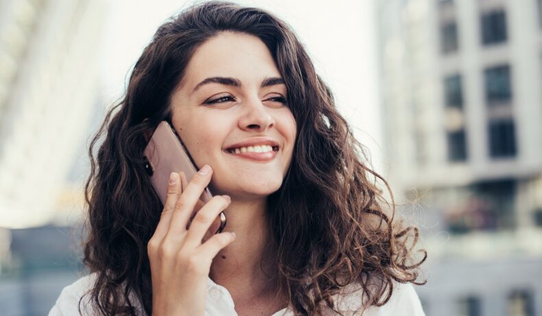 Femeie cu părul creț și închis la culoare, care vorbește la telefon, pentru a ilustra de ce nu sunt sigure conversațiile pe telefon