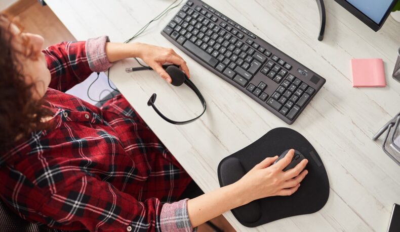 Persoană îmbrăcată în roșu care stă la un birou alb, cu mână pe un mouse negru și o tastatură neagră, pentru a ilustra modul în care folosești mouse-ul și tastatura