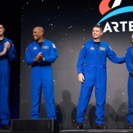 Astronauții Jeremy Hansen, Victor Glover, Reid Wiseman și Christina Hammock Koch, pe 3 aprilie 2023, în costume albastre, pe scenă când NASA a dezvăluit astronauții Artemis II