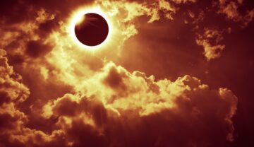 Eclipsă solară, înconjurată de nori, în nuanțe de portocaliu, similară cu o eclipsă solară hibridă foarte rară