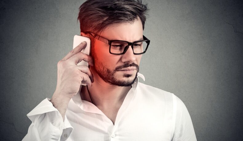 Bărbat cu ochelari, în cămașă albă, pe frundal gri, care vorbește la telefon, pentru a ilustra ce efect au telefoanele asupra creierului