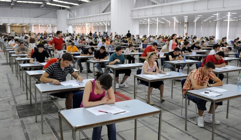 Oameni care sunt într-o sală de examen și care stau la birou pentru a da examenul, pentru a ilustra cele mai grele examene din lume