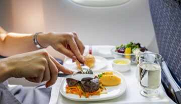 Pasager în avion care mănâncă mâncare cu cuțit și furculiță pentru a ilustra de ce are mâncarea gust diferit în aer