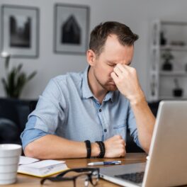 Bărbat care e nefericit la birou, cu un laptop în față, îmbrăcat cu o cămașă albastră, pentru a ilustra un bărbat care și-a dat demisia de la jobul lui