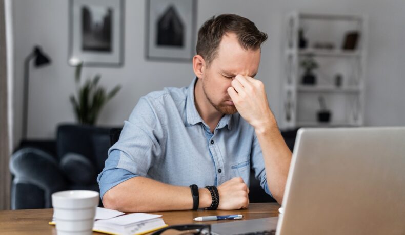 Bărbat care e nefericit la birou, cu un laptop în față, îmbrăcat cu o cămașă albastră, pentru a ilustra un bărbat care și-a dat demisia de la jobul lui