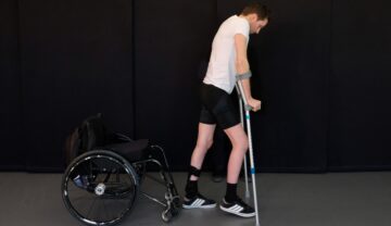 Gert-Jan Oskam, un bărbat paralizat care a putut merge din nou, pe fundal negru, în 2018, cu cârje în mâini și un tricou alb