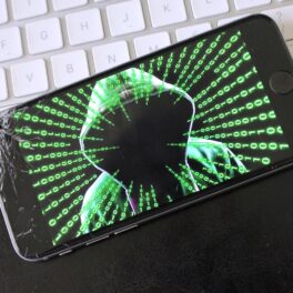 Telefon cu ecran negru, pe cacre e un hacker cu cod verde, pe o tastatură albă, pentru a ilustra virusul periculos care a infectat peste 400 de milioane de telefoane