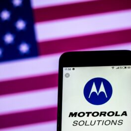 Motorola Solutions, afacerea Motorola care e mai profitabilă, pe ecranul unui telefon, cu steagul american pe fundal