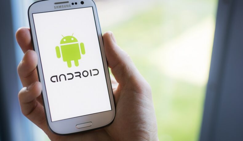 Telefon Android alb, cu simbolul pe ecran, ținut în mână de un utilizator, pentru a ilustra cum să ai mai mult spațiu pe telefon