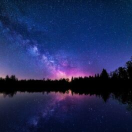 Cer întunecat de noapte, cu galaxie, deasupra unui lac, în nuanțe de albastru și roz, pentru a ilustra de ce e cerul întunecat noaptea