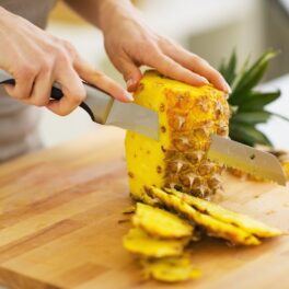 Persoană care taie un ananas pe un tocător din lemn, pentru a ilustra de ce te doare gura când mănânci ananas