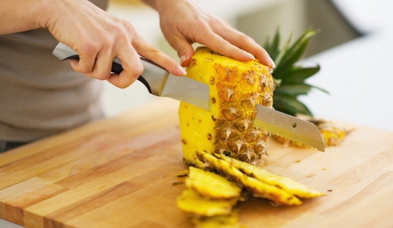 Persoană care taie un ananas pe un tocător din lemn, pentru a ilustra de ce te doare gura când mănânci ananas