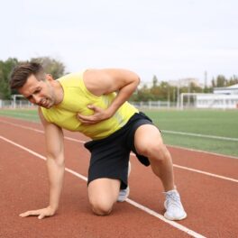 Bărbat tânăr, îmbrăcat sport, pe un teren de alergat, care se ține de piept, pentru a ilustra ziua în care au loc cele mai multe atacuri de cord