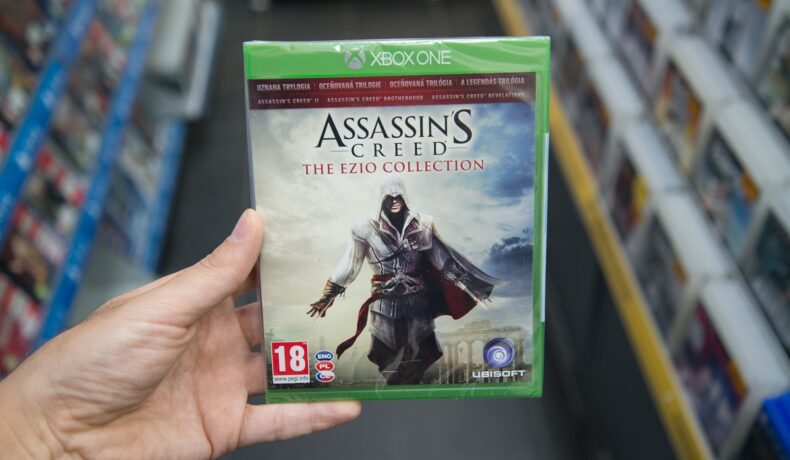 Utilizator care ține în mână o carcasă cu un joc Assassin's Creed, într-un magazin, pentru a ilustra că Ubisoft lansează Assassin’s Creed Nexus