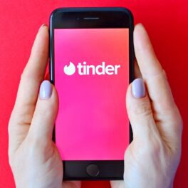 Utiliatoare care ține un telefon cu Tinder în mână, pe fundal roșu, entru a ilustra ce fac utilizatorii pe această aplicație