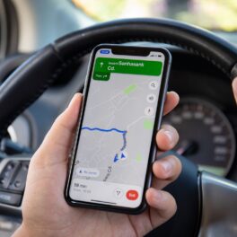 Utilizator aflat la volan care ține un telefon în mână cu o hartă, locația telefonelor iPhone poate fi și în Franța