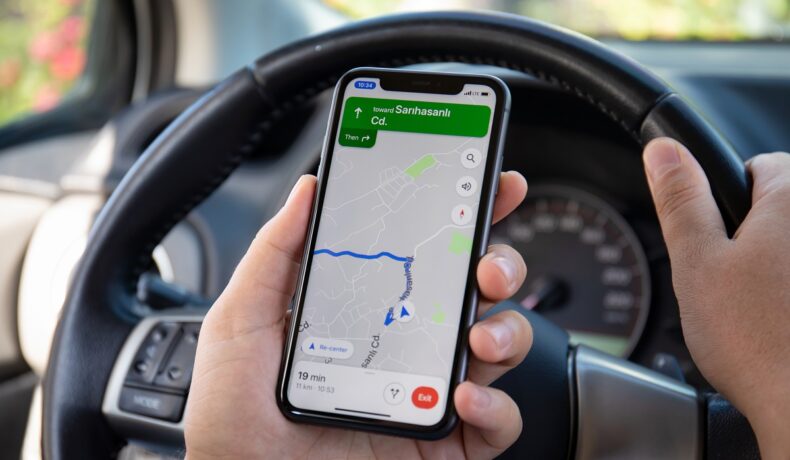 Utilizator aflat la volan care ține un telefon în mână cu o hartă, locația telefonelor iPhone poate fi și în Franța